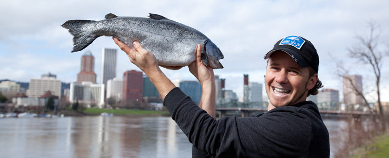 Lyf holding a salmon with Portland in the background
