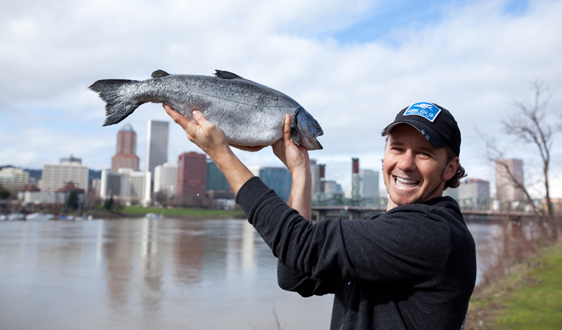 Lyf holding a salmon with Portland in the background